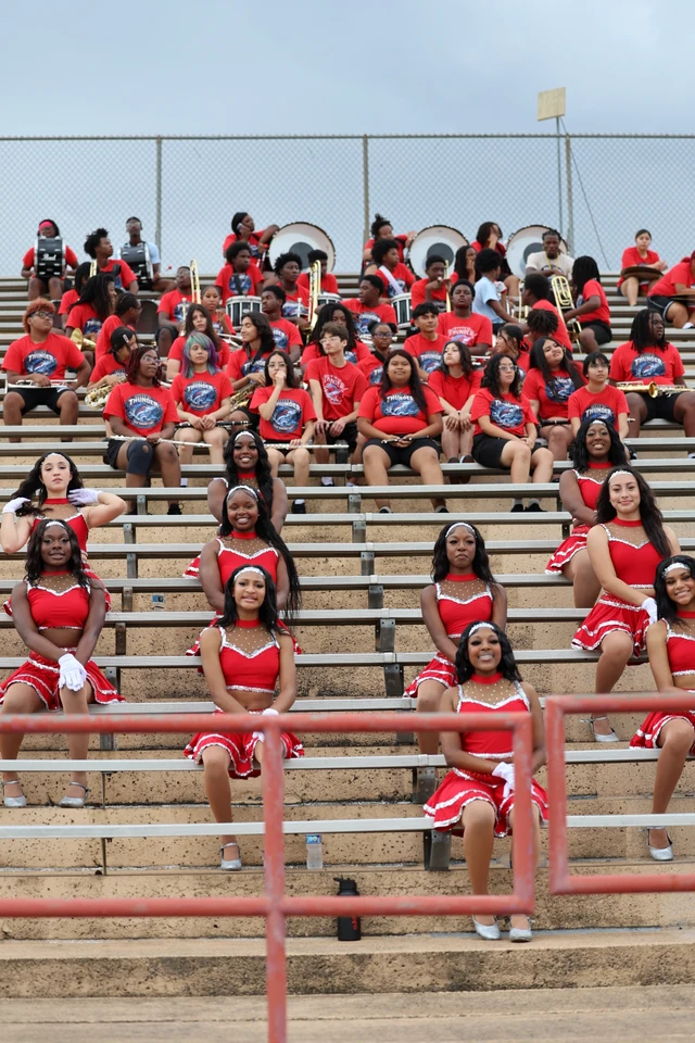 Dancers in red uniforms and band members with instruments seated across the stadium bleachers.